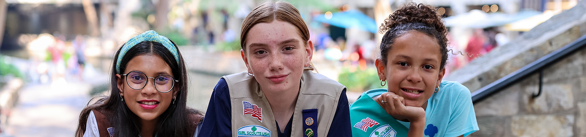  Three Girl Scouts leaning on a stone wall facing forward and smiling 