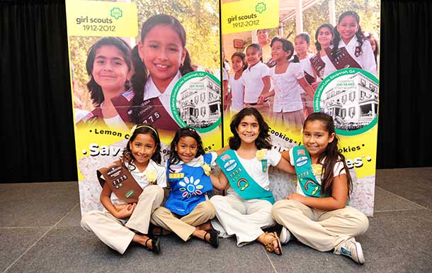 2010s image of young girl scouts in uniform sitting in front of big boxes of cookies
