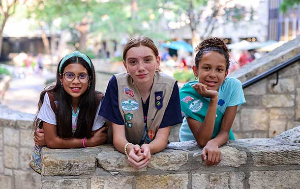 3 girl scouts at the riverwalk leaning on a bridge