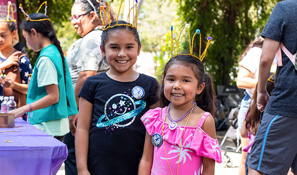 Two young girls with hand made crowns smiling at the day of the girl S.A. event