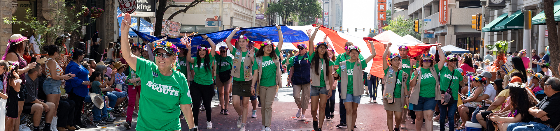  GSSWT CEO Angie Salinas marching in front of Girl Scouts holding up American flag in the Battle of Flowers parade 