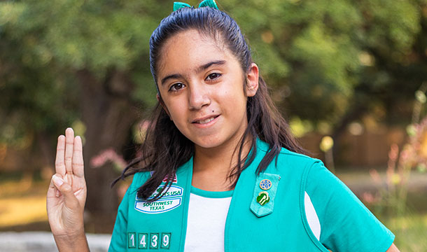 Girl Scout Junior en uniforme sosteniendo el símbolo de la mano de Girl Scout hacia arriba