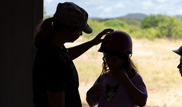 silhouette of camp counselor fixing the riding helmet of a girl for horse back riding