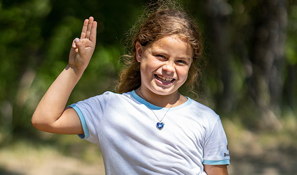 girl scout outside smiling and holding up girl scout promise sign