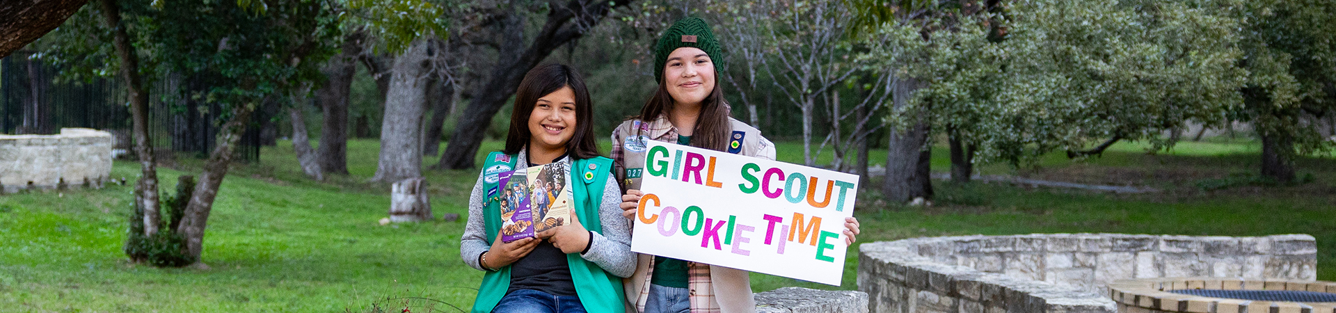  hands of young girl scout holding cookie box and handing it to a customer at an outdoor cookie booth 