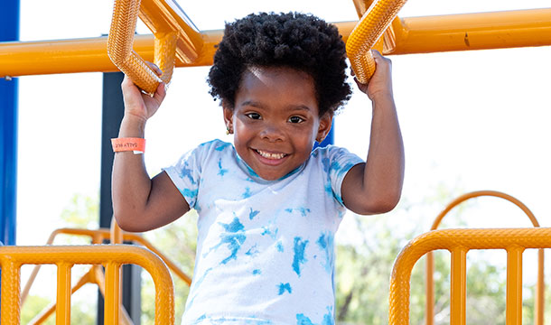 young girl scout outside hanging on monkey bars